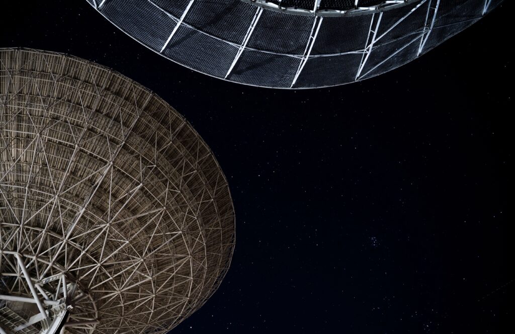 Large radio telescopes under a star-filled night sky supporting deep-space communication, radio astronomy, and global satellite infrastructure.