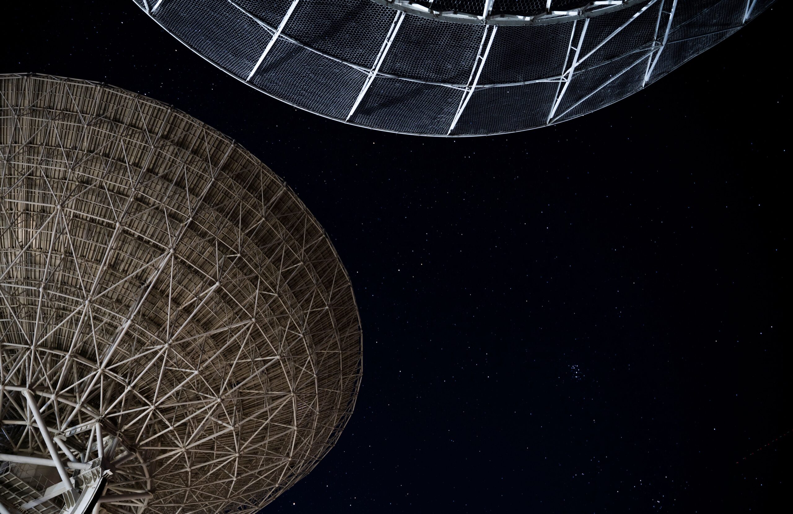 Large radio telescopes under a star-filled night sky supporting deep-space communication, radio astronomy, and global satellite infrastructure.