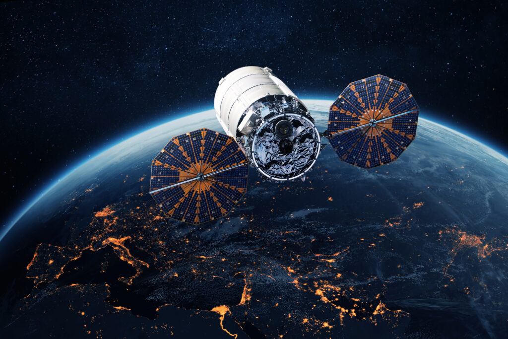 Satellite with extended solar panels orbiting above Earth at night, illustrating space infrastructure and satellite technology.